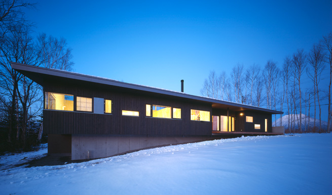 南西よりの外観夕景。雪原に窓が重なる平屋が浮かぶ。