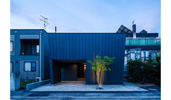 道路よりの外観夕景。中庭の塀と外壁が一体となった、ストイックな外観。