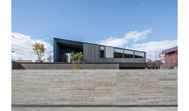 道路よりの南東側外観。羽目板転写コンクリート塀の内側に横長のコートが拡がる。